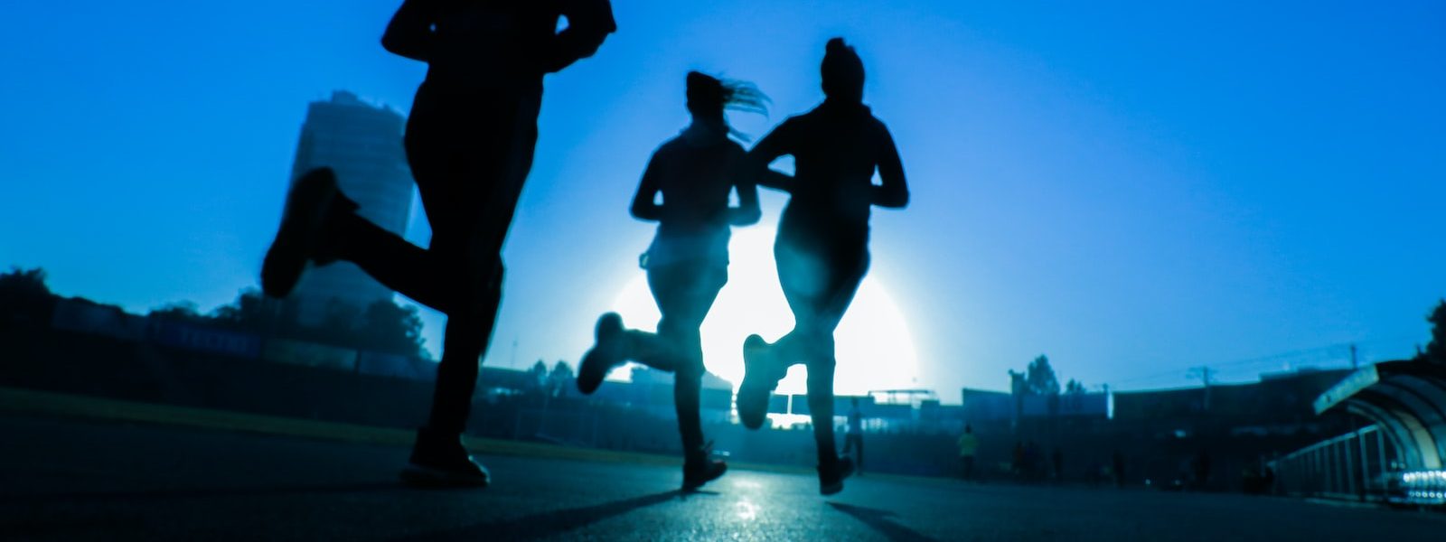 silhouette of three women running on grey concrete road